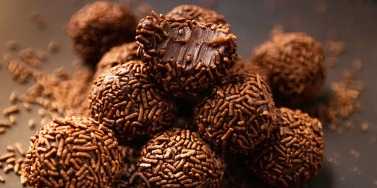 Brigadeiros de café empilhados com granulado, um deles mordido mostrando o recheio cremoso