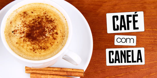 Xícara de café com canela em pó polvilhada sobre a espuma e paus de canela no pires, vista de cima, sobre mesa de madeira