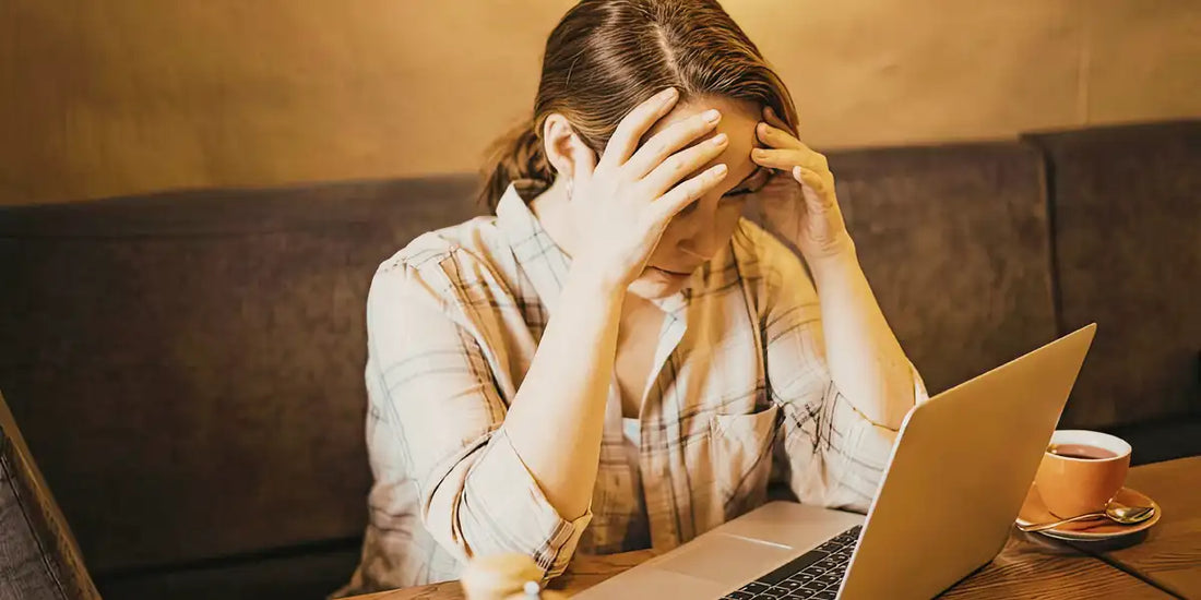 essoa apoiando a cabeça nas mãos diante do laptop, com uma xícara de café ao lado