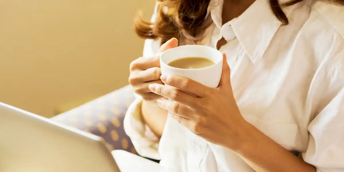 Mulher segurando uma xícara de café com as duas mãos, em clima de conforto e tranquilidade
