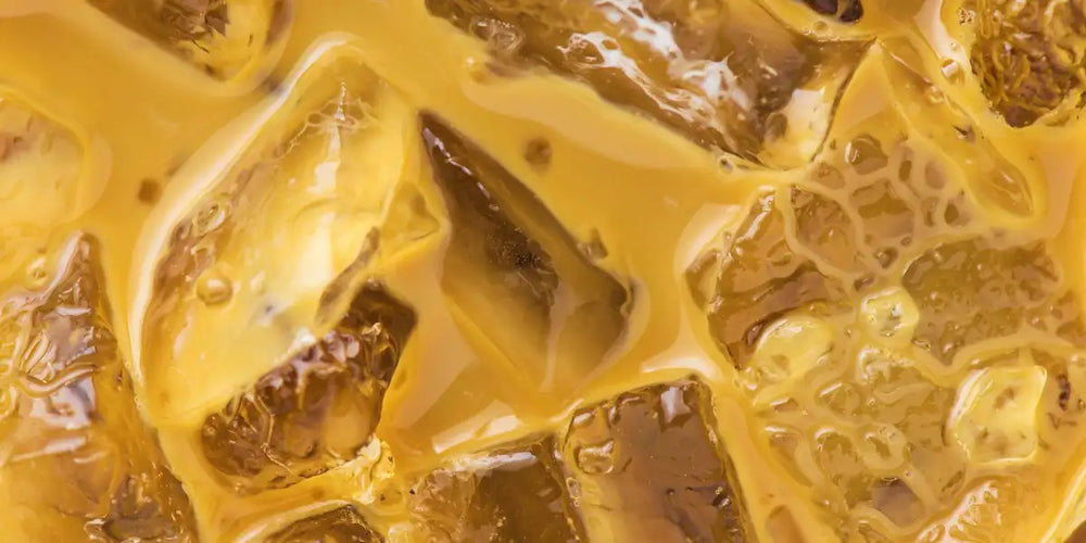 Macro de café gelado cremoso e dourado com cubos de gelo translúcidos e reflexos de luz