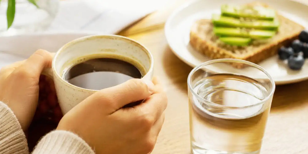 Pessoa segurando xícara de café ao lado de um copo de água, representando dicas para café sem desconforto