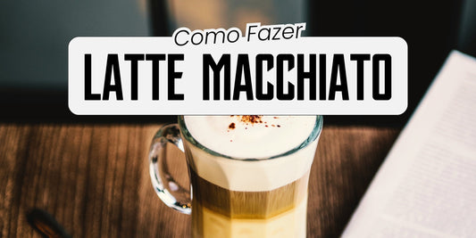 Latte macchiato em copo de vidro com camadas de leite, café e espuma polvilhada com canela sobre mesa de madeira