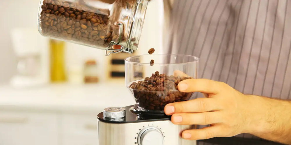Pessoa abastecendo moedor de café elétrico com grãos frescos