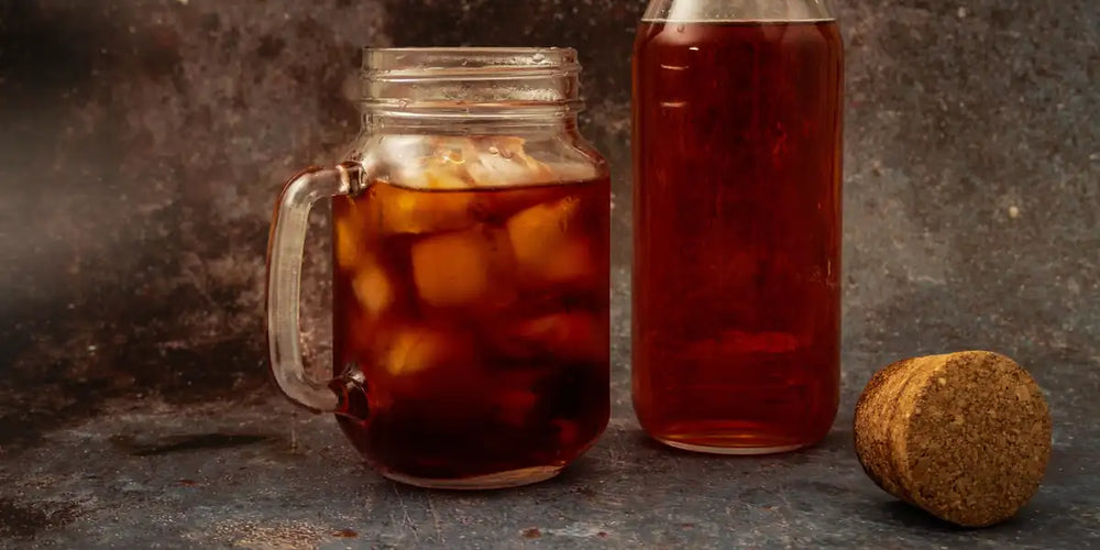 Caneca de vidro com cold brew e gelo ao lado de garrafa com concentrado de café e rolha de cortiça