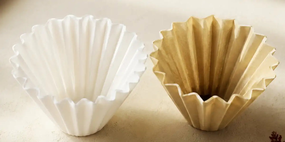 Filtro de papel branco ao lado de filtro de papel pardo sobre fundo claro, comparação lado a lado