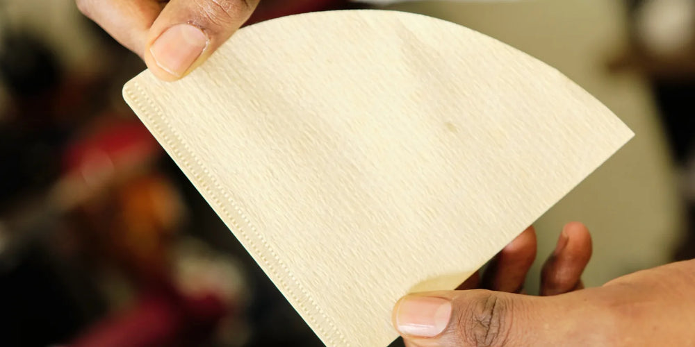Mãos segurando filtro de papel V60 cônico natural, com a borda pregueada visível