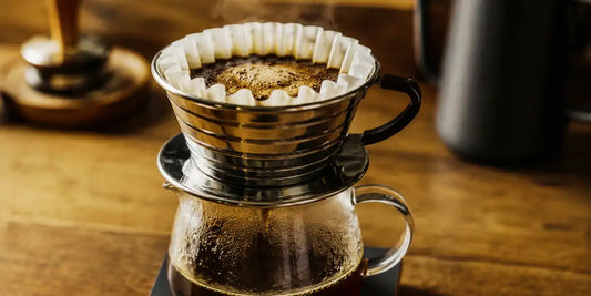 Coador Kalita Wave de aço inox preparando café coado sobre jarra de vidro, com vapor subindo