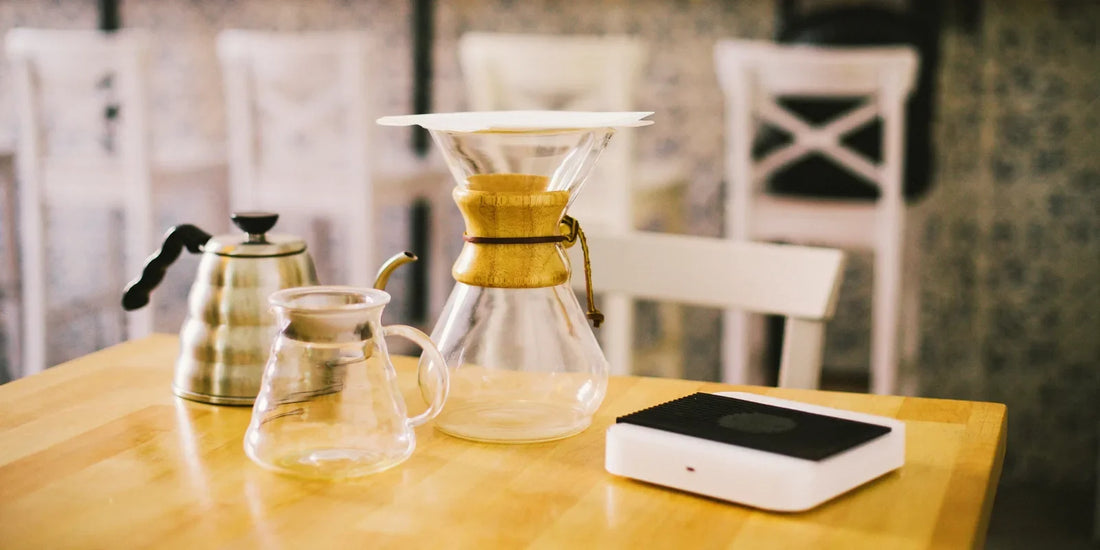 Kit de café equilibrado com chaleira, jarra de vidro, Chemex e balança sobre mesa de madeira