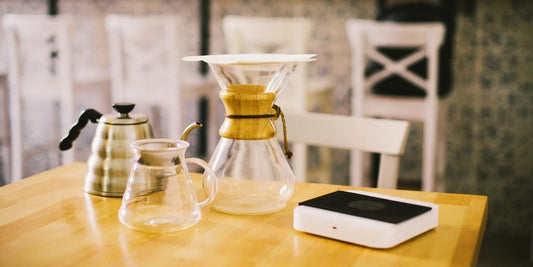 Kit de café equilibrado com chaleira, jarra de vidro, Chemex e balança sobre mesa de madeira