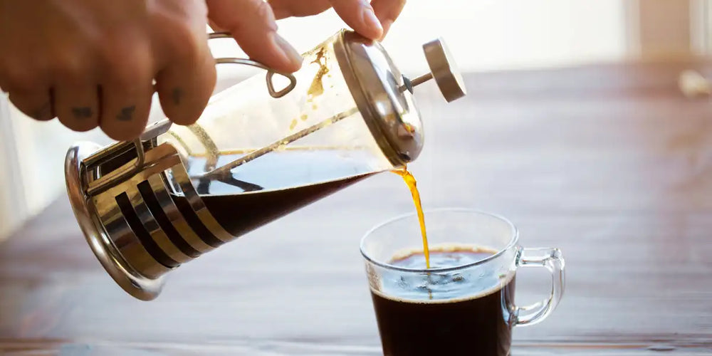 Prensa francesa de vidro com café sendo pressionado na cozinha
