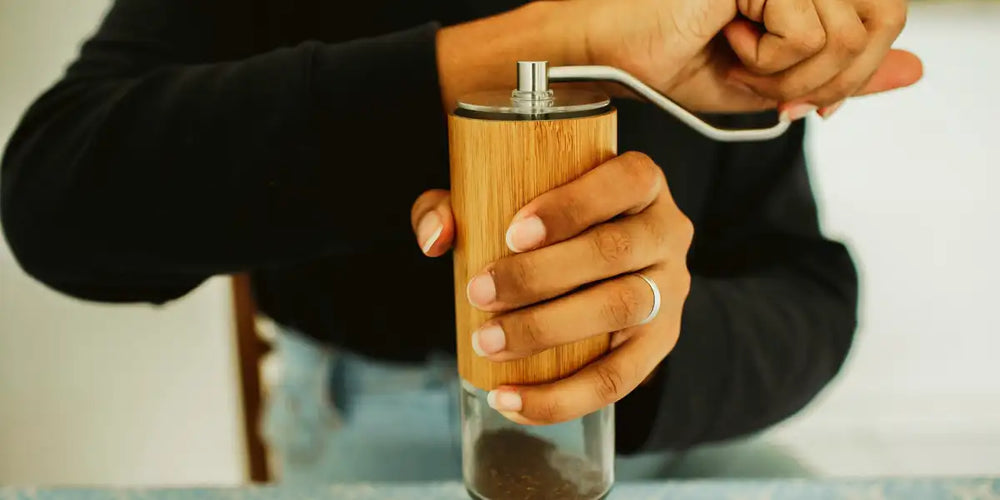 Mãos girando a manivela de um moedor manual de café com corpo de bambu