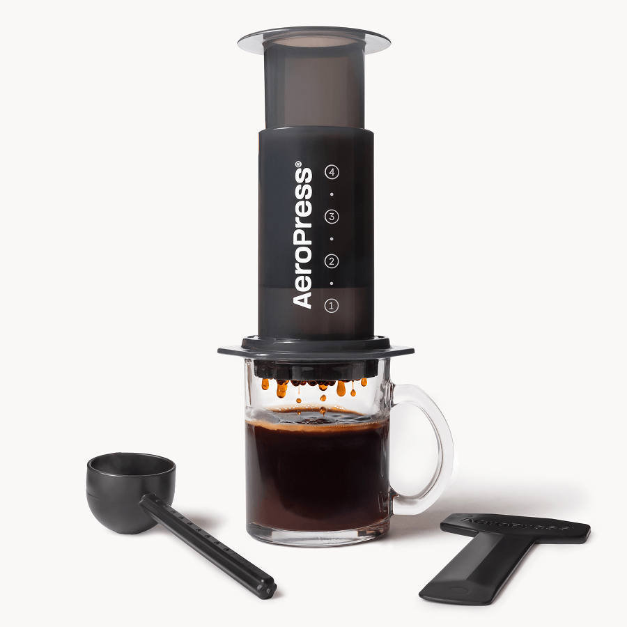 AeroPress Original preparando café sobre caneca de vidro, com colher medidora e pá para mexer
