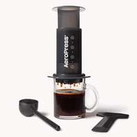 AeroPress Original preparando café sobre caneca de vidro, com colher medidora e pá para mexer
