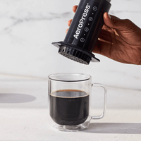 AeroPress Original na mão ao lado de uma caneca de café pronto