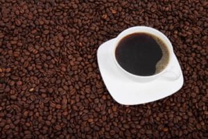 imagem de uma xícara branca com café preto, em cima de vários grãos de café